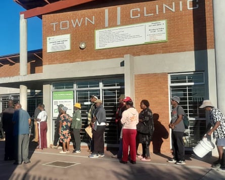 African men and women stand outside a brick building marked “Town II clinic”