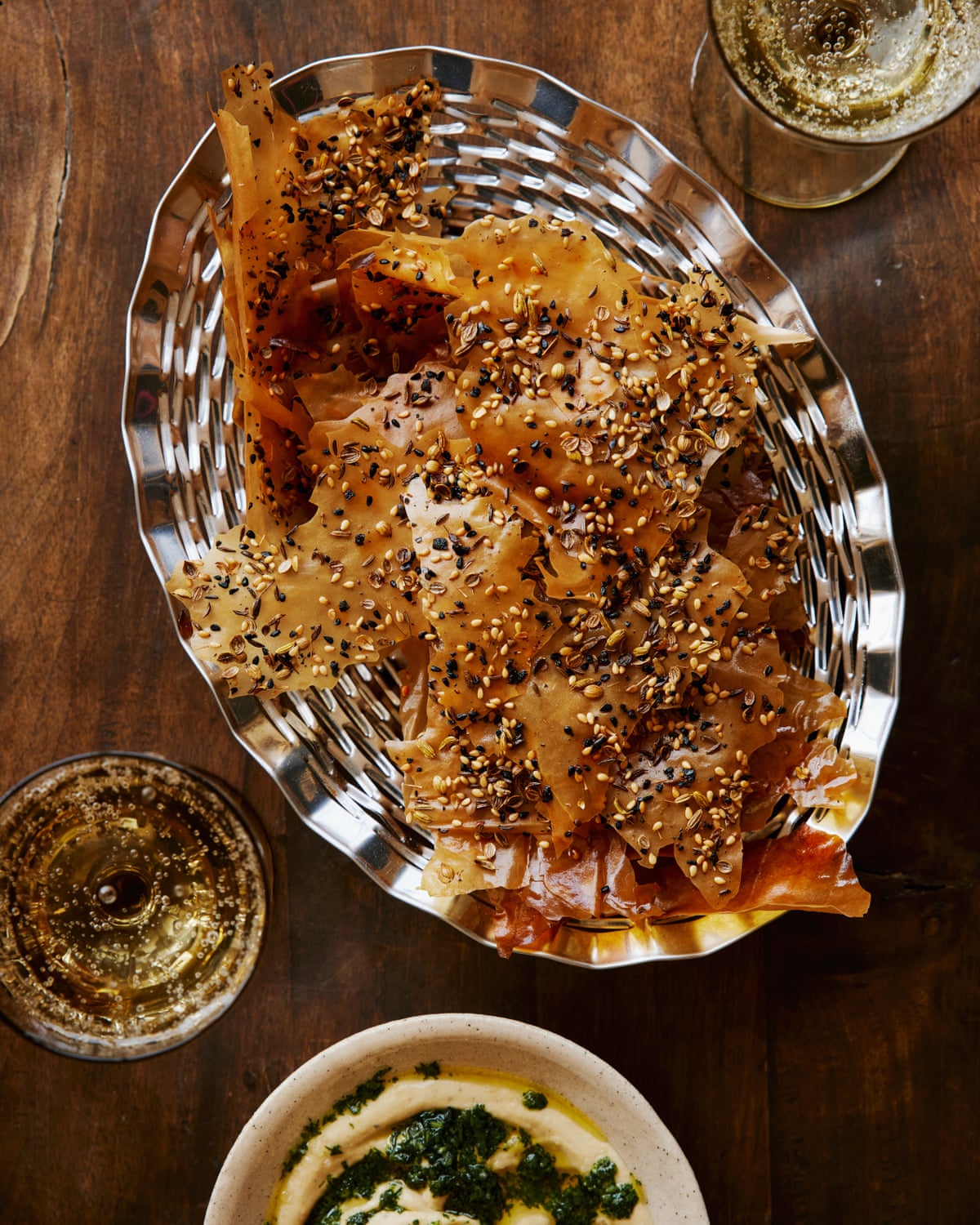 seeded filo crackers in a metal dish with dips and drinks alongside