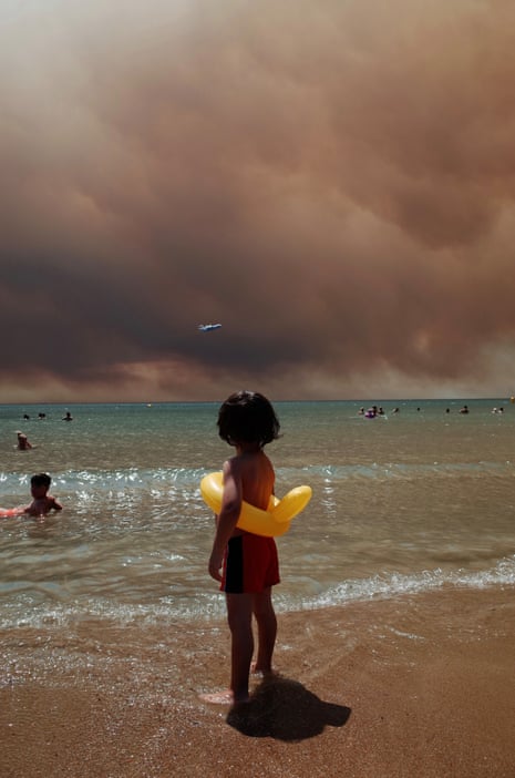 A child on a beach watches smoke from wildfires in Turkey.