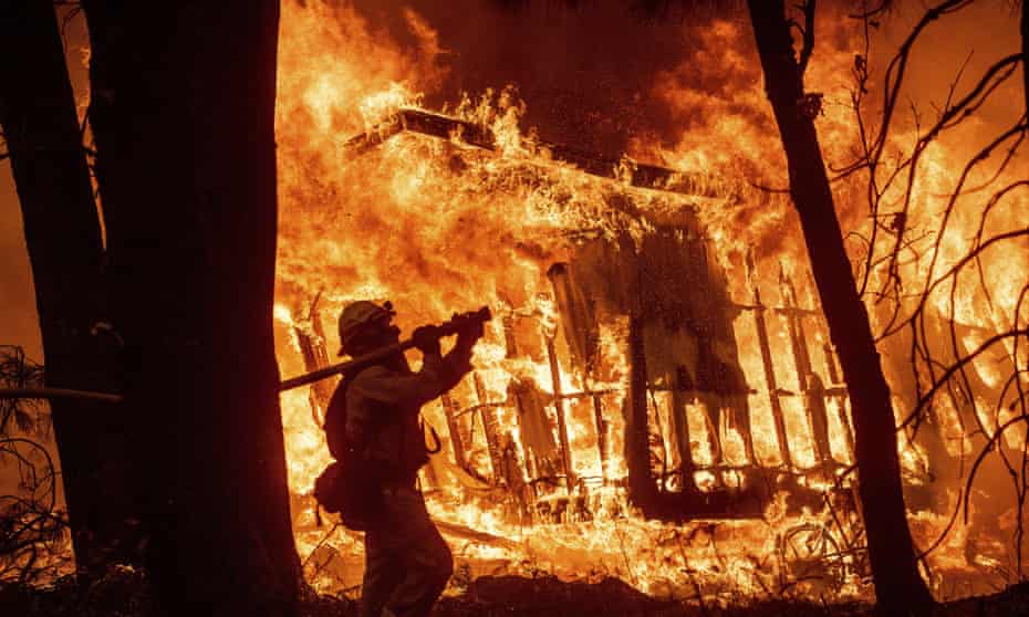 A firefighter sprays water as flames from the Camp Fire consume a home in Magalia, California in 2018