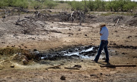 A conservation official holds his shirt over his nose as he approaches an oil-sheened pond created by an abandoned well in Pecos County.
