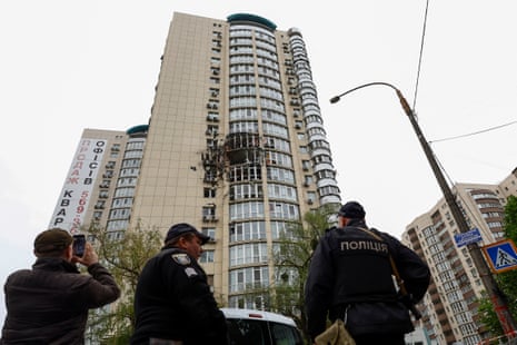 Police officers stand next to an apartment building damaged by the remains of a drone shot down over Kyiv.