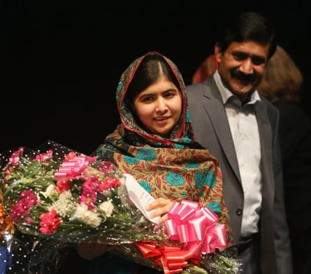 A young woman holds a large bouquet while a man smiles beside her.