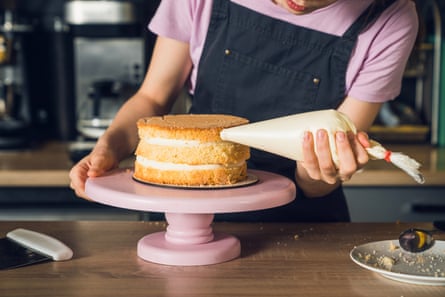 Woman’s hands in black apron decorate cake, squeezes out vanilla cream on a side of a cake