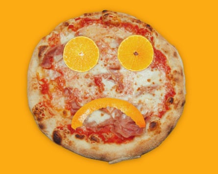 A pizza with slices of orange peel and rind making a sad face