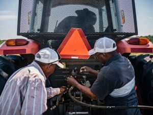 Farm assistants Ernest Lambert, left, and Ira Gregory, right, hook up the cables for a disc harrow to John Boyd Jr’s new tractor.