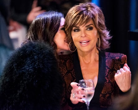 a woman whispers in another woman’s ear