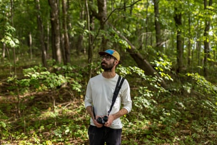 Vincent Moreau stands in a forest holding binoculars