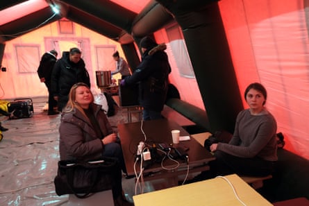 Two women at a table with plugs in power sockets inside a red tent.