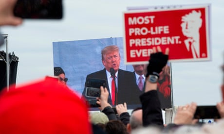 Donald Trump is shown on a screen speaking to a crowd as a person holds a sign reading 'Most pro-life president ever'.