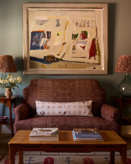 A painting by Elizabeth Blackadder hangs in a living room. There is a two-seater sofa, a coffee table and two side tables with lamps on.