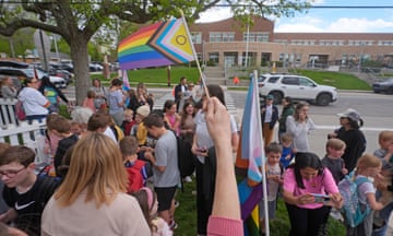 Parents and kids gather in front of a school with a trans rights flag.