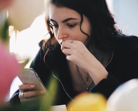 A teenage girl sits scrolling on her phone