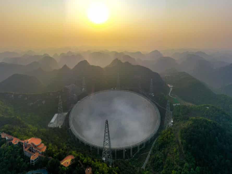 Misty tree-covered mountains surround the huge concave dish of the 500-metre Aperture Spherical Radio Telescope in China.