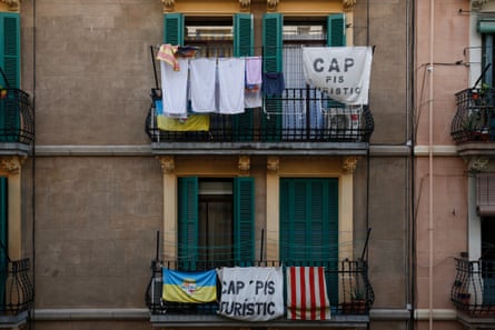 Banners reading ‘no tourist flats’ hang from balconies on the frontage of an old building, alongside laundry and regional flags; there are dark green wooden shutters at the windows.