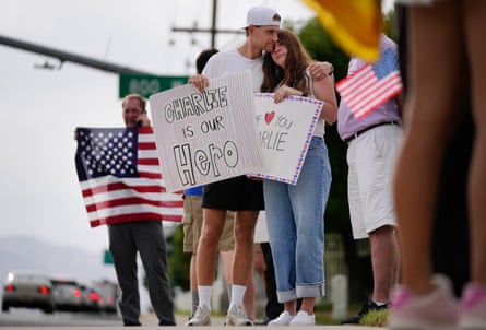 A young couple embrace while holding signs that say ‘Charlie is our hero’