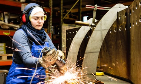 Young female trainee works with a grinder in a workshop, flying sparks