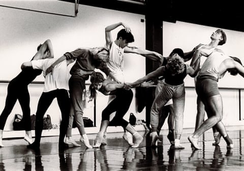A black and white photograph of a group of dancers tilting their bodies and linking arms
