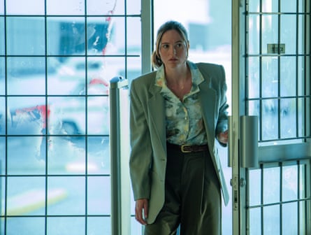 A woman going through a square glassed door, looking worried. Cars are in the background