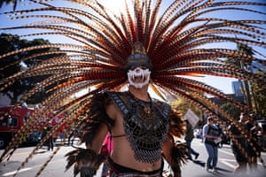 A man wears a feathered headdress and a skull mask