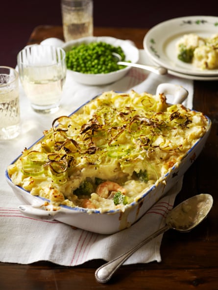Fish pie shown on a table with plates, glasses and a bowl of peas nearby.