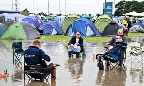 Festivalgoers sit in a water at a camping area after heavy rains hit Roskilde Festival