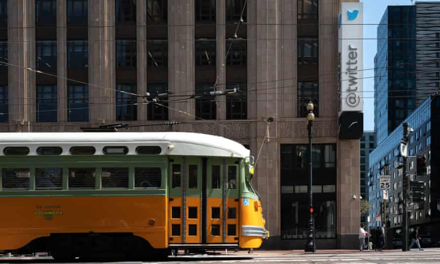 A yellow and green streetcar traveling along the street in front of an imposing old office building with '@twitter' running vertically along a sign at its corner