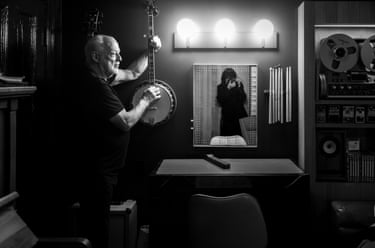 Samson is seen photographing in a mirror while Gilmour raises a stringed instrument