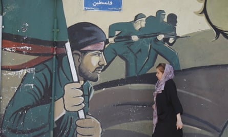 A woman walks next to a wall painting of Iranian Revolutionary Guards