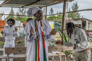 Rastafarians in white costume clap their hands as they stand in an open-sided temple