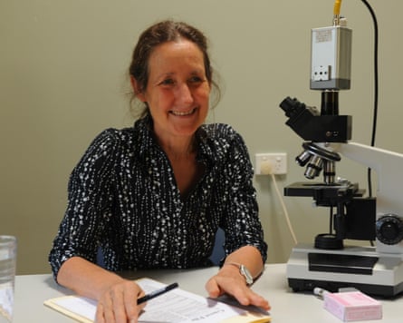 A woman sitting at a desk in a black and white blouse with a microscope on her right