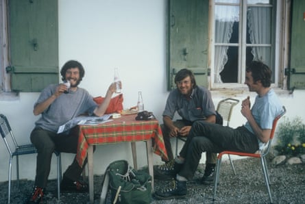 Three men sitting at a table outside an Alpine building with shutters on the windows