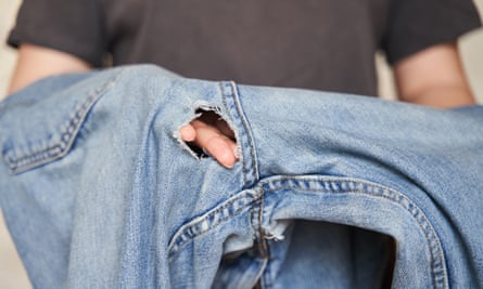 Man’s arms holding jeans with hole near the crotch seam.