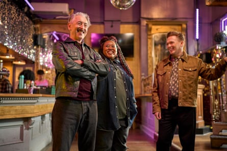 Two men and a woman stand in a bar smiling