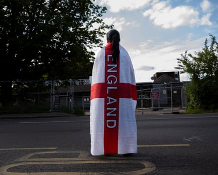 A woman draped in an England flag stands in the road opposite a closed-down hotel