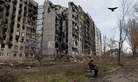 A resident sits in front of Mariupol apartment blocks destroyed in the fighting