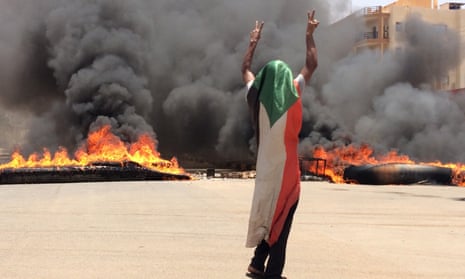 A protester wearing a Sudanese flag flashes the victory sign in front of burning tires and debris in Khartoum, Sudan.