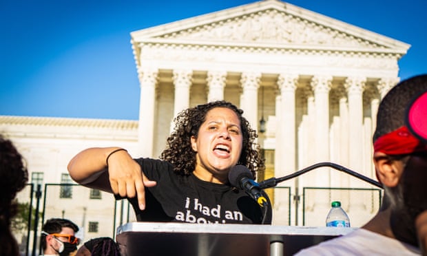 A woman speaks into a microphone at a podium set up in front of temporary black fencing surrounding the US supreme court building.