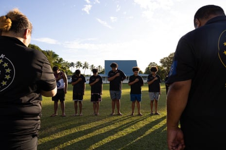 Young people standing outdoors with their heads bowed and hands on their hearts in Rarotonga