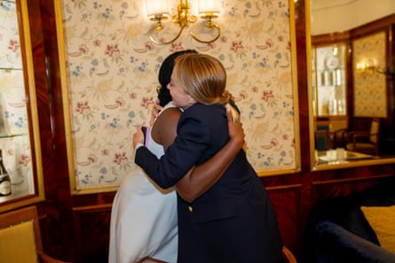Kemi Badenoch and Giorgia Meloni hug each other tightly in a traditional-style Rome cafe with dark wooden panels and flowered wallpaper.