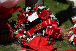 A wreath of red red roses and smaller white flowers and a red ribbon with the words ‘RIP Diogo’ rests in front a red bucket hat with writing on the brim
