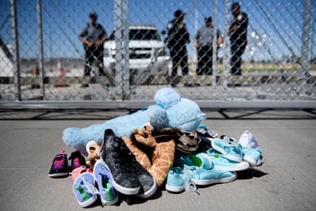 Shoes and toys in front of a chain-link fence with uniformed men looking on.