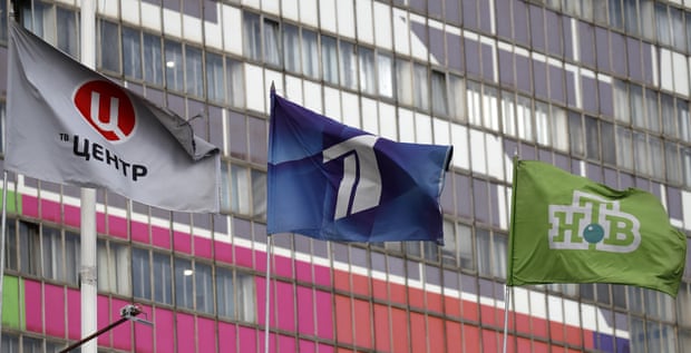 Three flags fly in front of a high-rise building.
