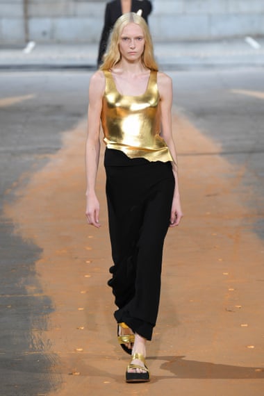 A model in a gold sleeveless vest structured like armour and a long black skirt on the Gabriela Hearst spring 2023 runway