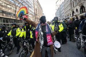 a person holds a fan bearing the colors of the Pride flag, a Planned Parenthood scarf around their neck and several police officers behind them