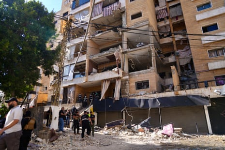 Rescuers work at a heavily damaged multi-story building with collapsed balconies and rubble on the street