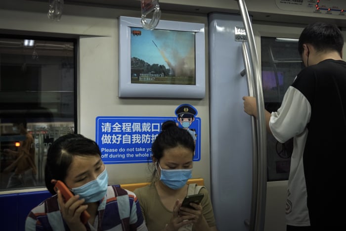 Commuters wearing face masks ride on a subway train as a TV screen shows China’s CCTV footage.
