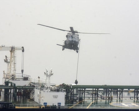 A soldier descends from a rope attached to the helicopter on to the deck of an oil tanker