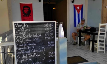 A tourist has a drink next to a Cuban flag and a poster depicting Che Guevara at a restaurant in Viñales, Pinar del Rio province, Cuba.