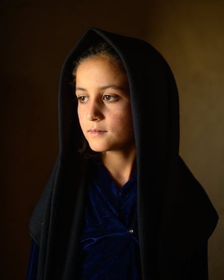 A solemn young girl in a headscarf looks off to one side